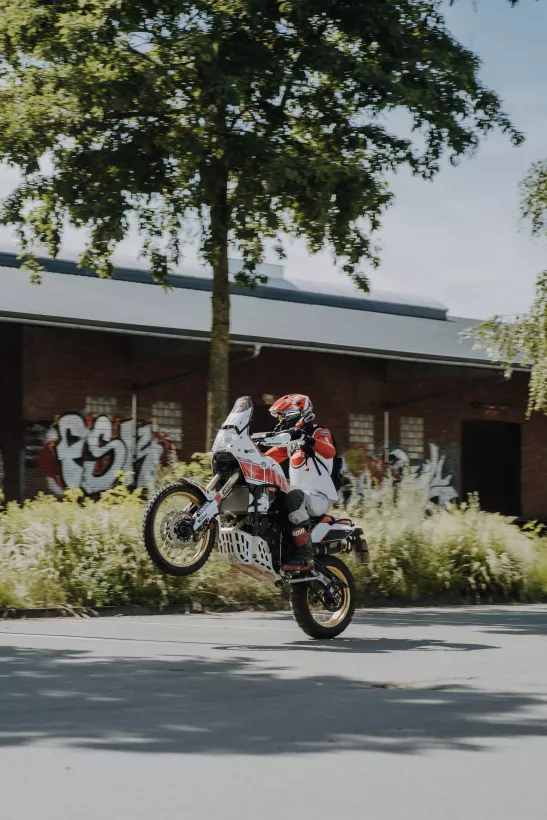 Actionfotografie eines Motorradfahrers beim Wheelie vor einer urbanen Kulisse mit Graffiti