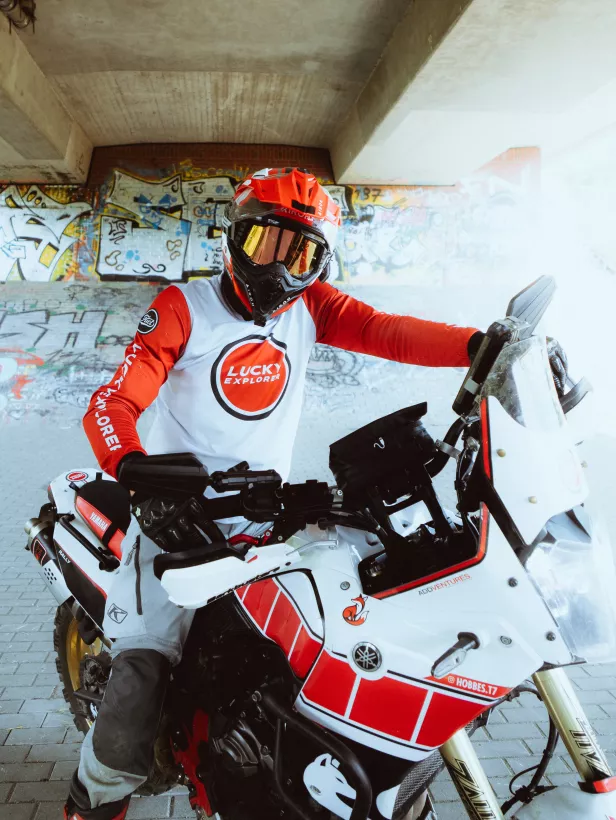 Actionfoto eines Motorradfahrers in roter Ausrüstung auf einem weißen Adventure-Bike vor einer Graffiti-Wand