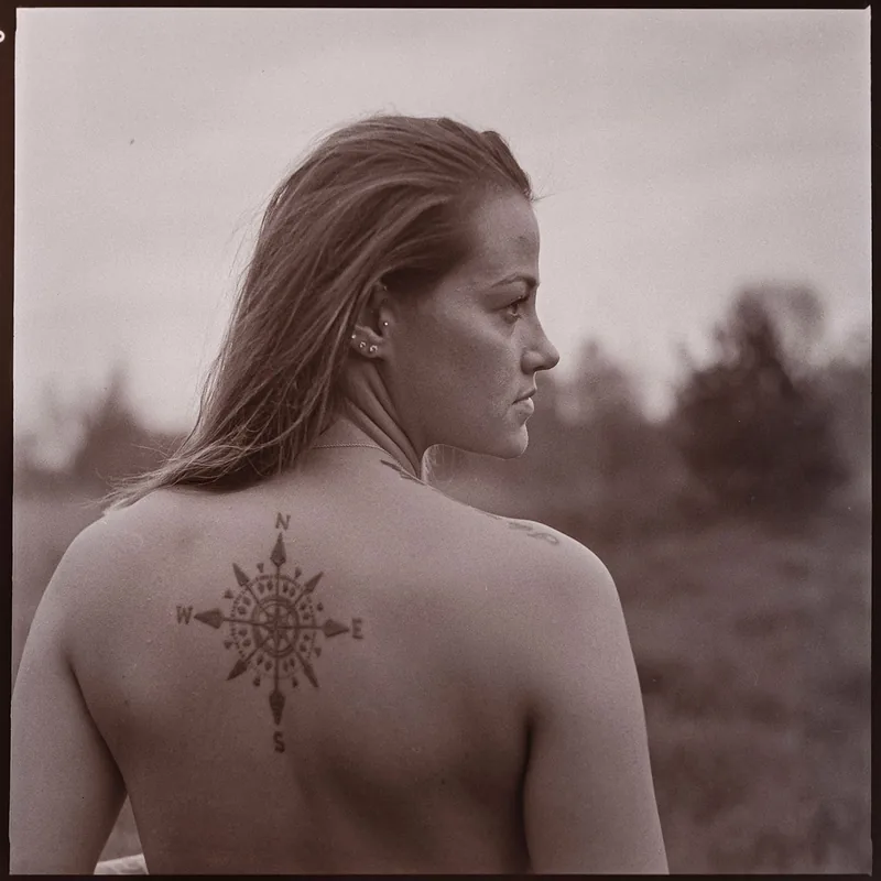 Analoges Porträt einer Frau im Profil mit einem Kompass-Tattoo auf dem Rücken.