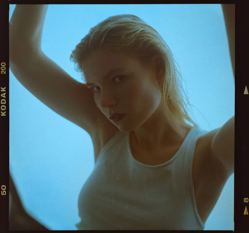 Analoges Portrait einer blonden Frau mit erhobenen Armen in einem weißen Top.