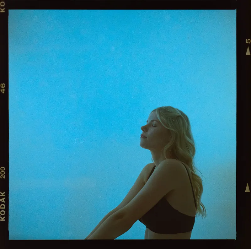 Analoges Portrait einer blonden Frau mit geschlossenen Augen vor blauem Himmel.