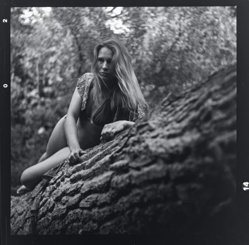 Analoges Schwarz-Weiß-Portrait einer Frau an einem Baumstamm im Wald