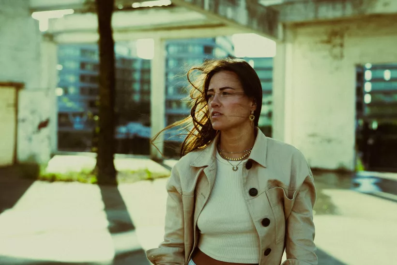 Analoges Portrait einer Frau in beiger Jacke vor urbaner Architektur