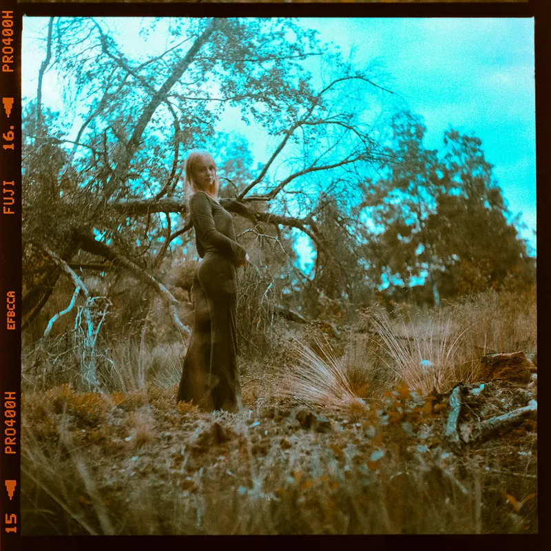 Analoges Portrait einer Frau mit blonden Haaren in einem langen dunklen Kleid im Wald.
