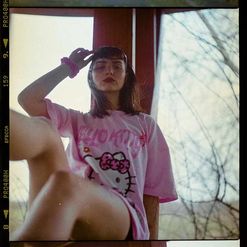 Analoges Portrait einer Frau mit dunklem Haar und rosa Hello Kitty T-Shirt.