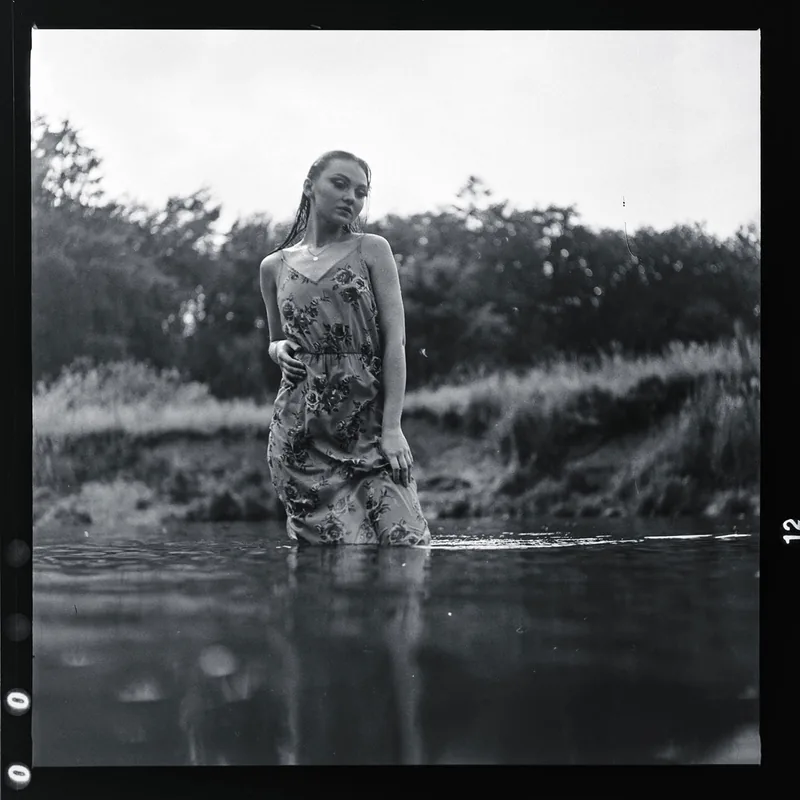 Analoges Portrait einer Frau in einem floralen Kleid, die in einem Fluss steht.
