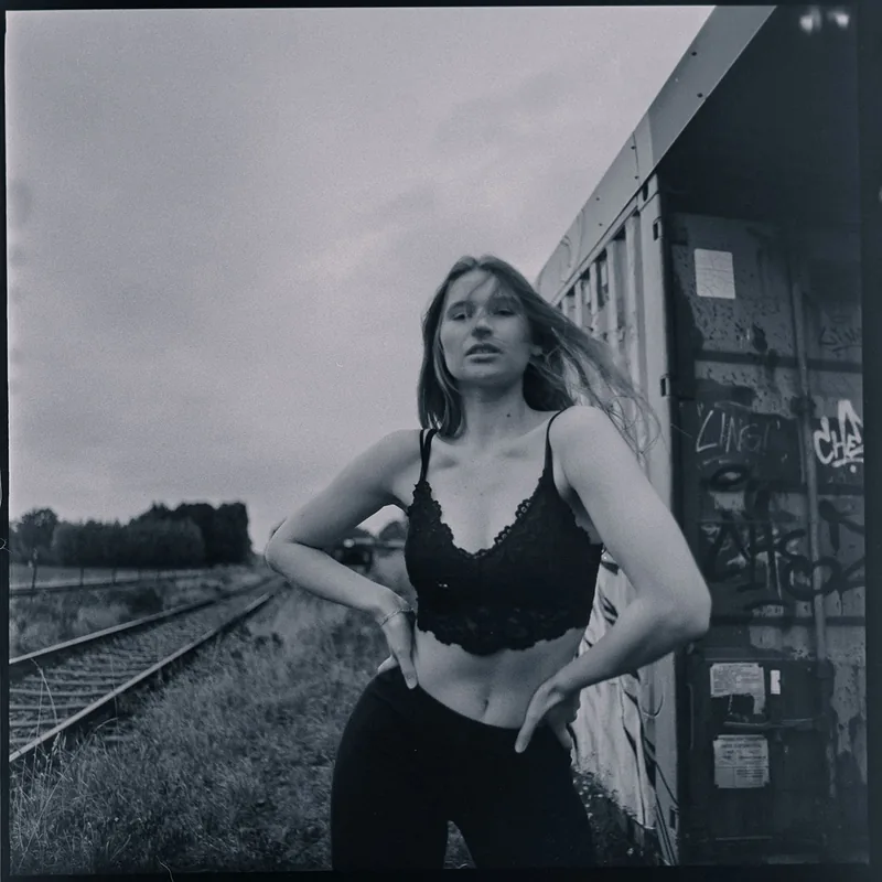 Analoges Portrait einer Frau vor einem mit Graffiti verzierten Waggon an Bahngleisen.