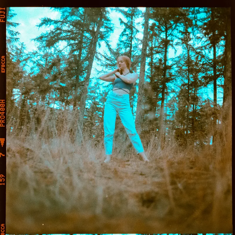 Analoges Portrait einer Frau in hellblauer Hose und grauem Top im Wald.