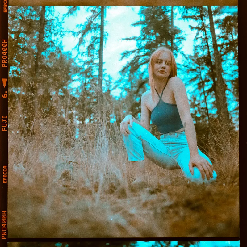 Analoges Portrait einer Frau, die im hohen Gras eines Waldes sitzt.
