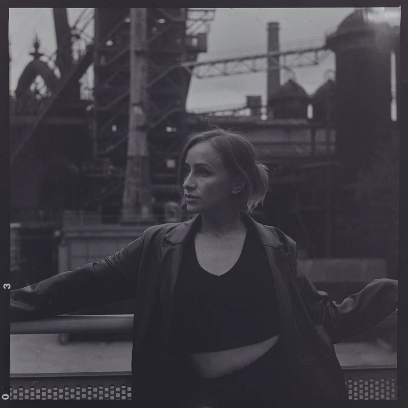Analoges Portrait einer Frau vor einer industriellen Kulisse mit Metallstrukturen.
