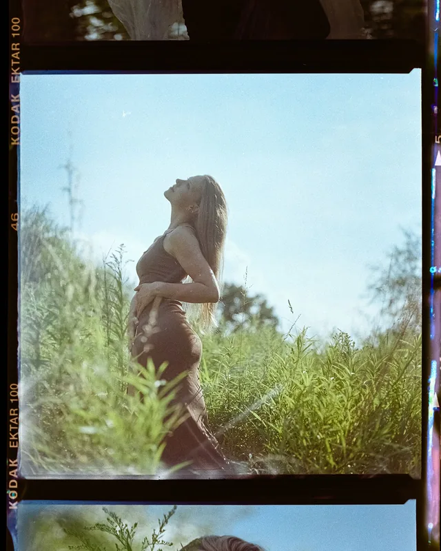 Analoges Portrait einer Frau im Profil, die in einer hohen Wiese zum Himmel aufblickt.