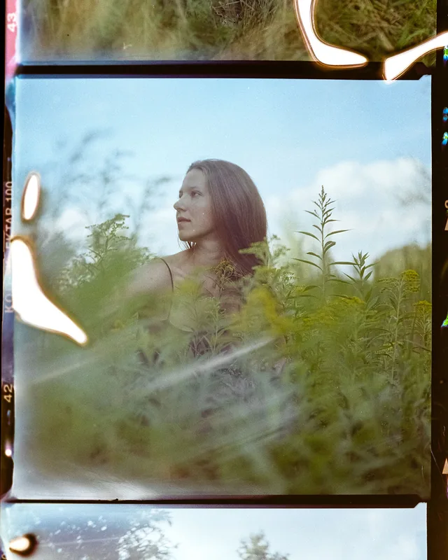 Analoges Portrait einer Frau im Profil inmitten von hohem Grün unter blauem Himmel.