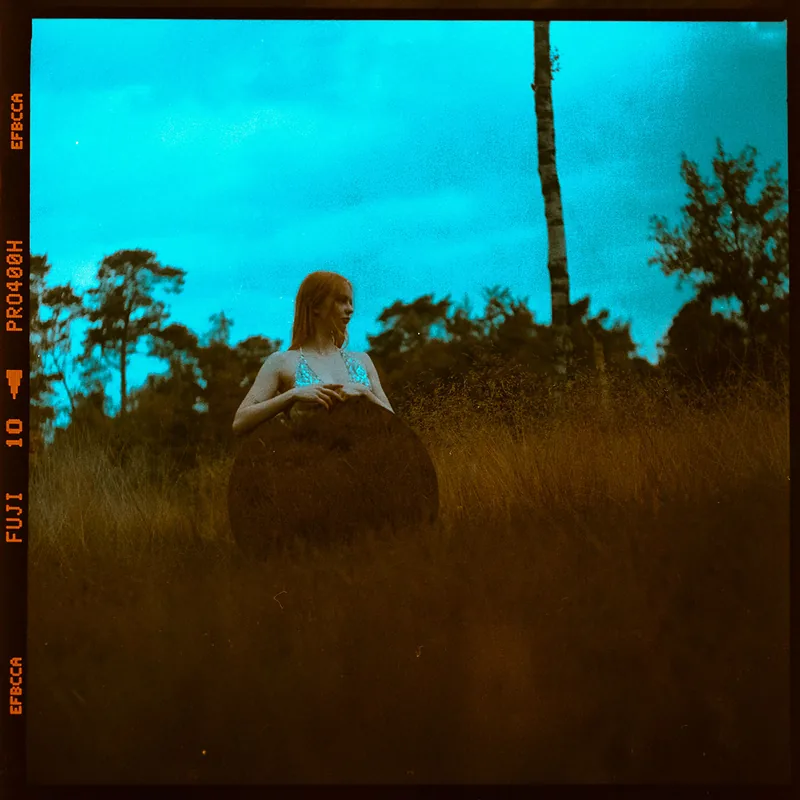 Analoges Portrait einer Frau mit rötlichem Haar in einer Wiese unter blauem Abendhimmel.