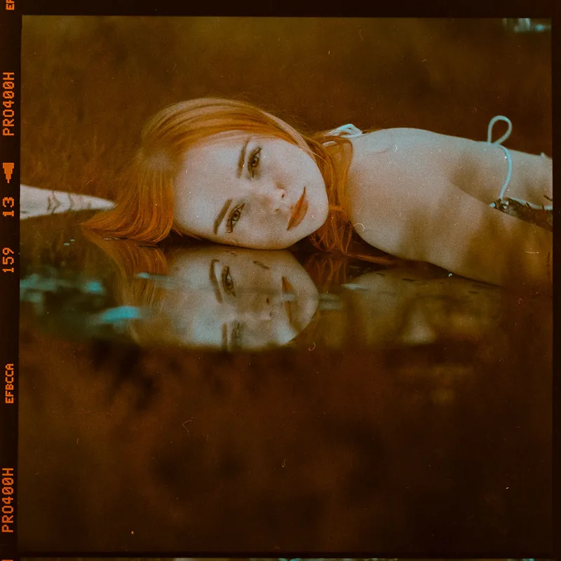 Analoges Portrait einer Frau mit rotem Haar, deren Gesicht sich im dunklen Wasser spiegelt.