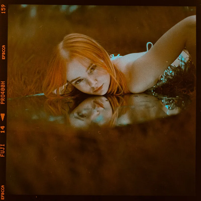 Analoges Portrait einer Frau mit rotem Haar und der Spiegelung ihres Gesichts im Wasser.