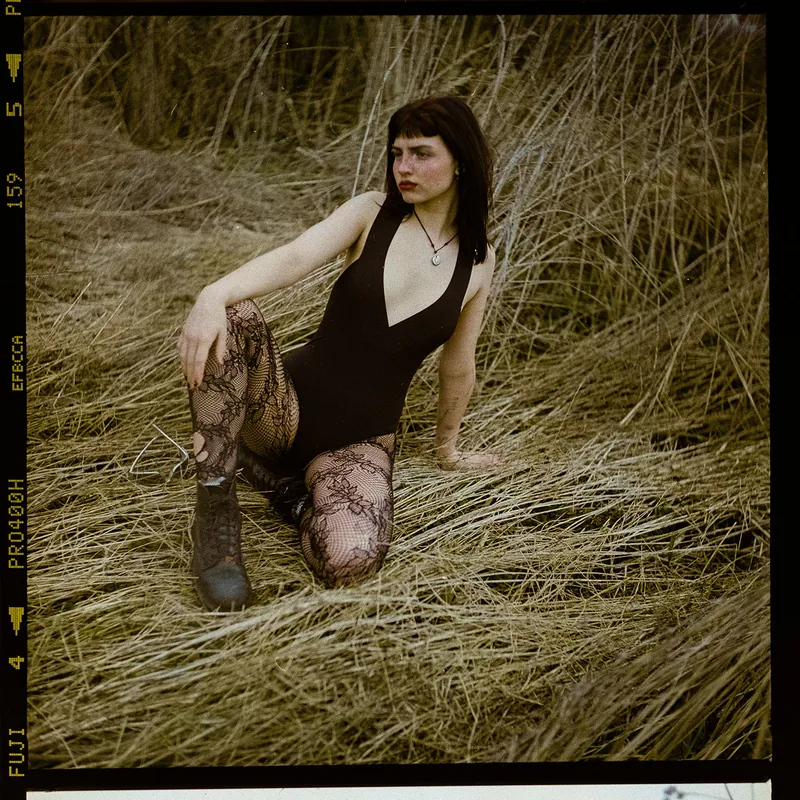 Analoges Portrait einer Frau in schwarzem Body und Spitzenstrumpfhosen im hohen Gras.