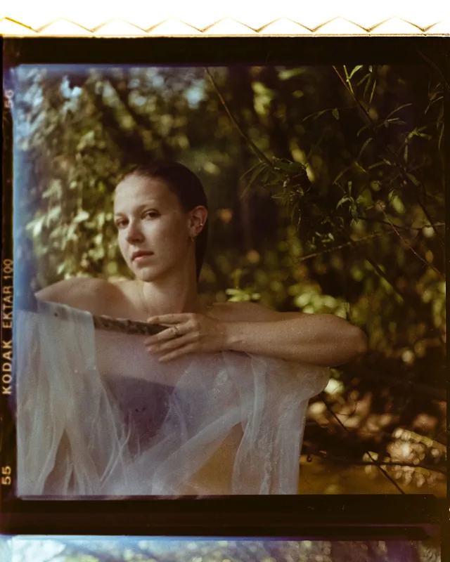 Analoges Portrait einer Frau in einem Wald mit weißem, transparentem Stoff.