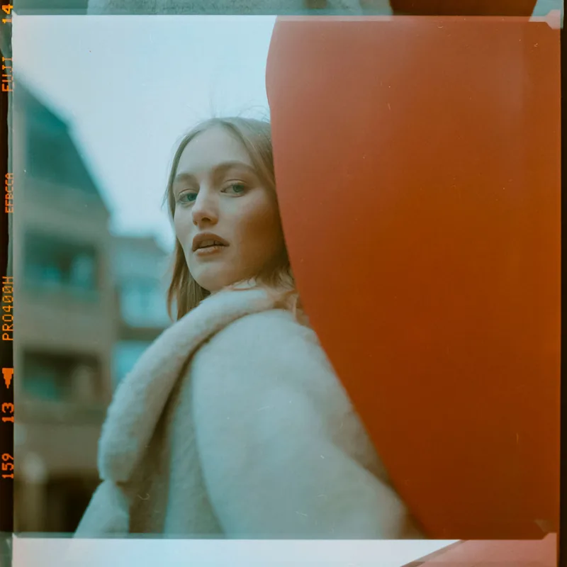 Analoges Portrait einer Frau im weißen Pelzmantel hinter einem großen roten Element