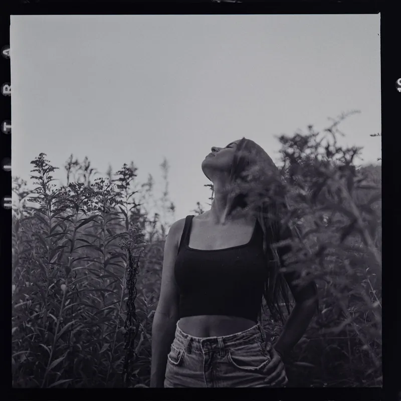 Analoges Portrait einer Frau, die zwischen hohem Gras zum Himmel blickt.