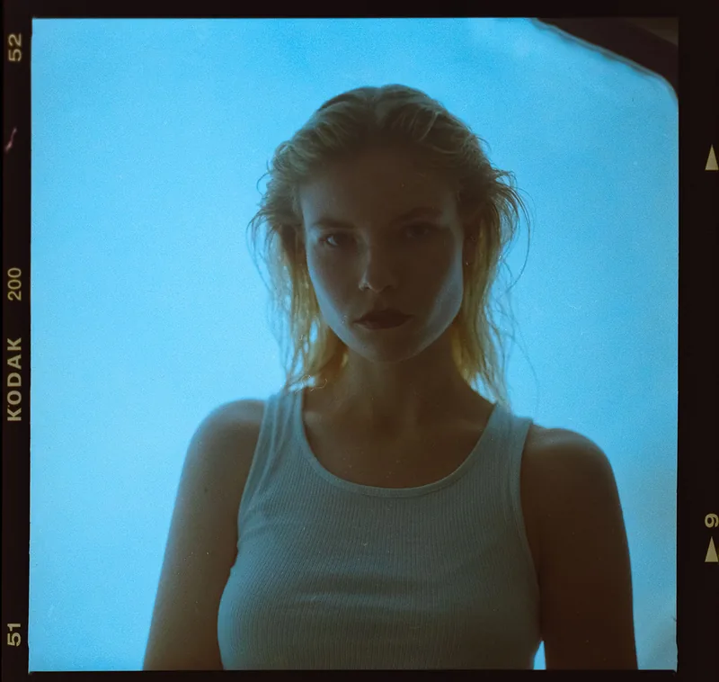 Analoges Portrait einer jungen Frau mit blondem Haar vor blauem Hintergrund