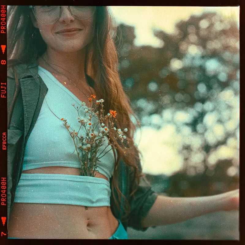 Analoges Portrait einer jungen Frau mit Brille und kleinen Wildblumen.