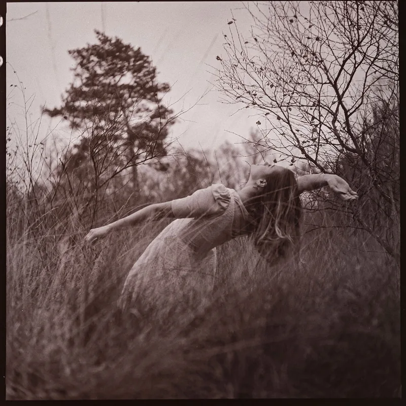 Analoges Portrait einer Person mit ausgestreckten Armen in einem Feld mit hohem Gras.