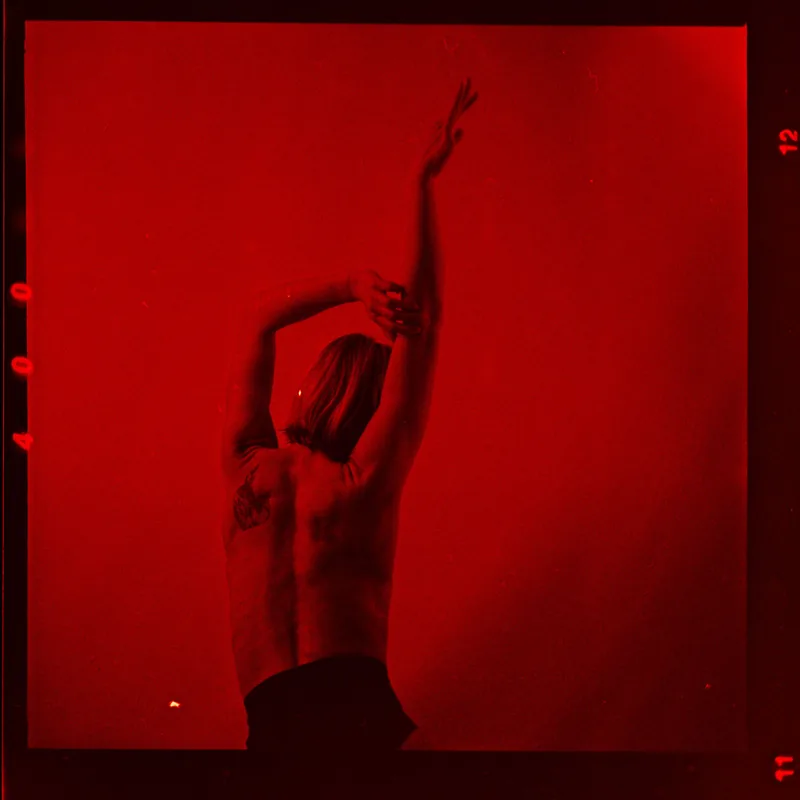 Analoges Portrait einer Person mit erhobenen Armen in intensivem Rot.
