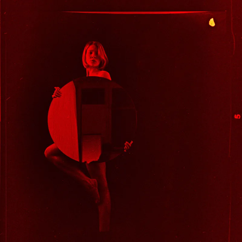 Analoges Portrait einer Person hinter einem großen runden Objekt in roter Beleuchtung.