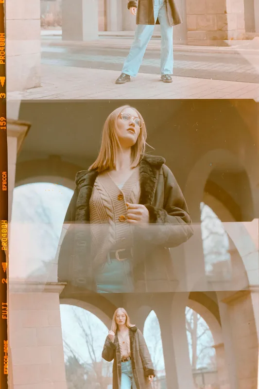 Analoges Portrait-Set einer blonden Frau in einem dunklen Mantel vor steinernen Bögen.