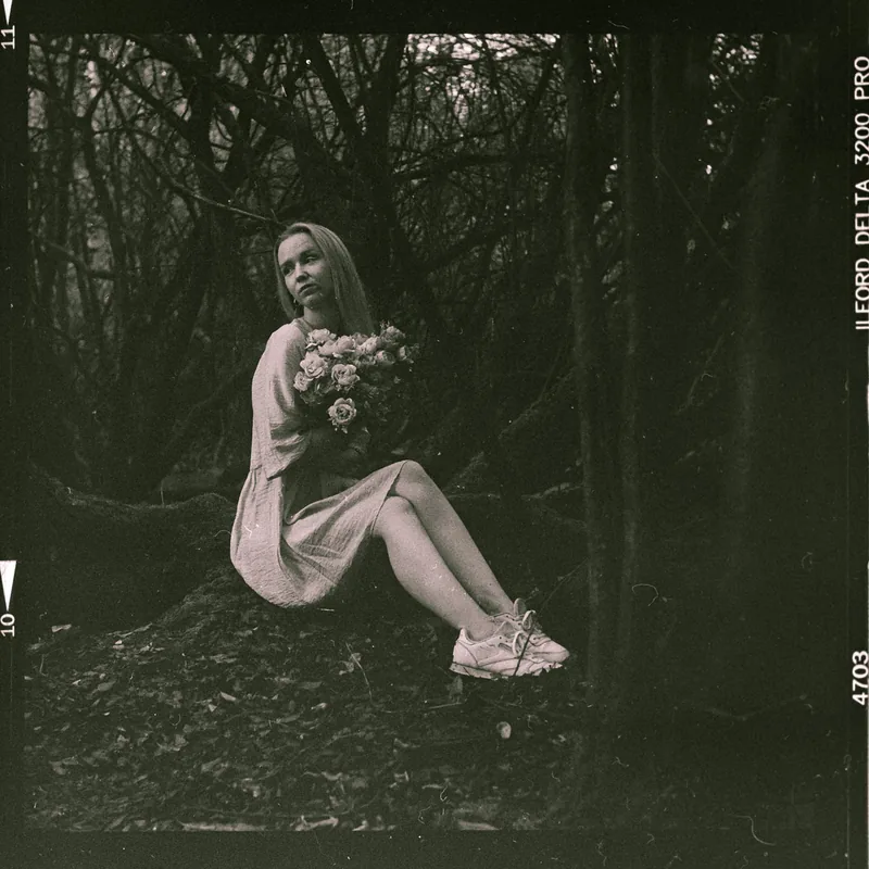 Analoges Portrait einer sitzenden Frau mit Blumenstrauß im Wald.