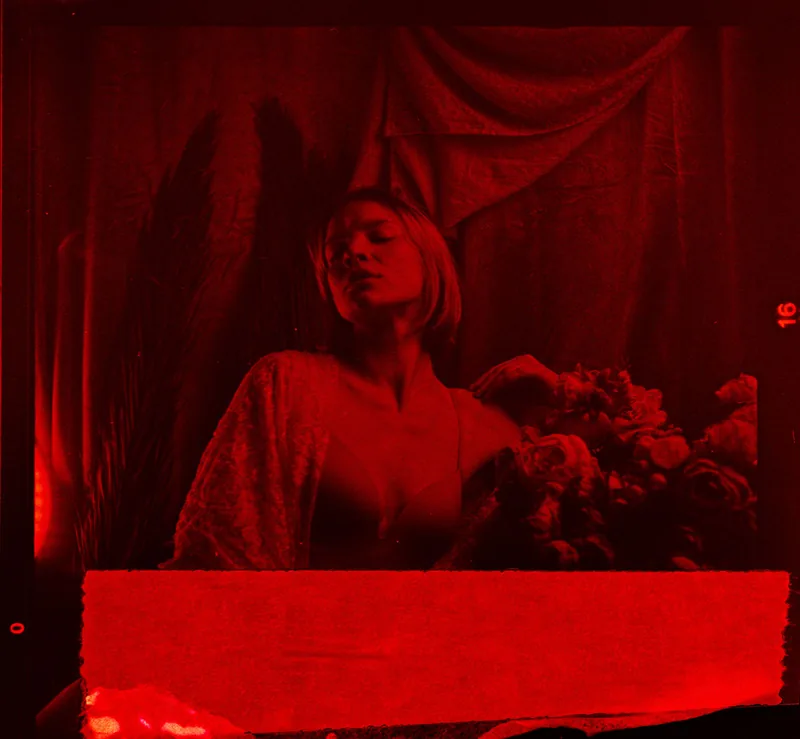 Analoges, rot getöntes Portrait einer Person mit nach hinten geneigtem Kopf und Blumen.
