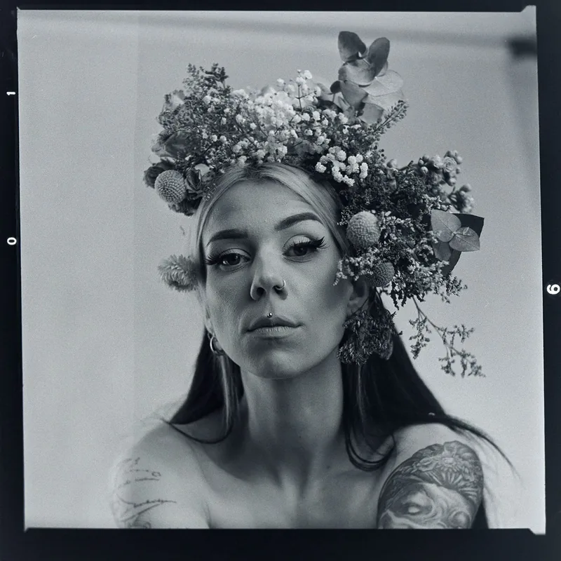 Analoges Schwarz-Weiß-Porträt einer Person mit einem üppigen Blumenkranz.