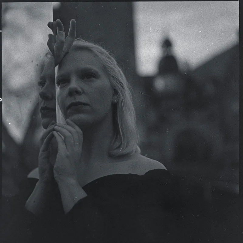Analoges Schwarz-Weiß-Portrait einer blonden Frau mit den Händen vor dem Gesicht.