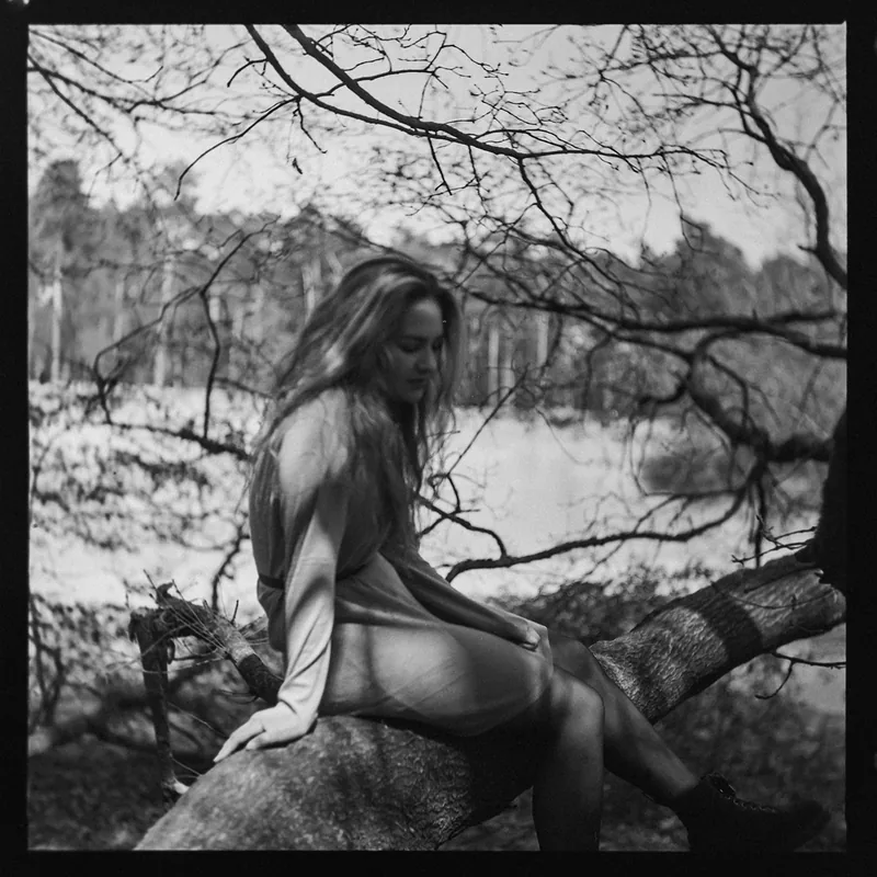 Analoges Schwarz-Weiß-Portrait einer Frau, die auf einem Baumast im Wald sitzt.