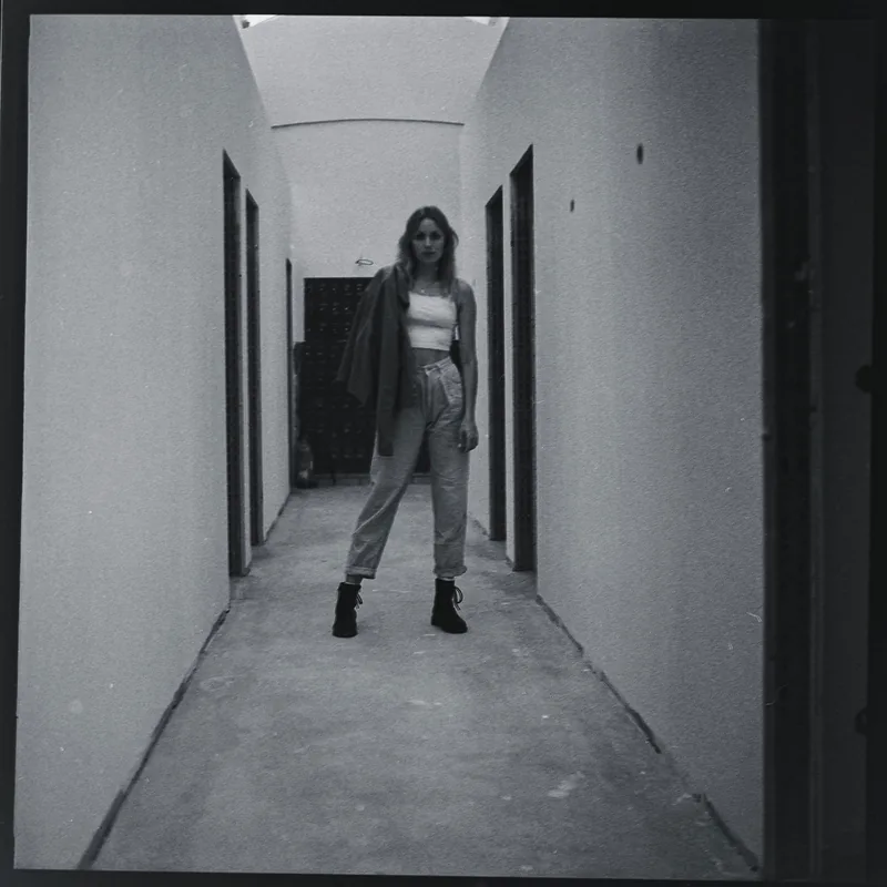 Analoges Schwarz-Weiß-Portrait einer Frau in einem hellen Flur mit weißem Top und heller Hose.