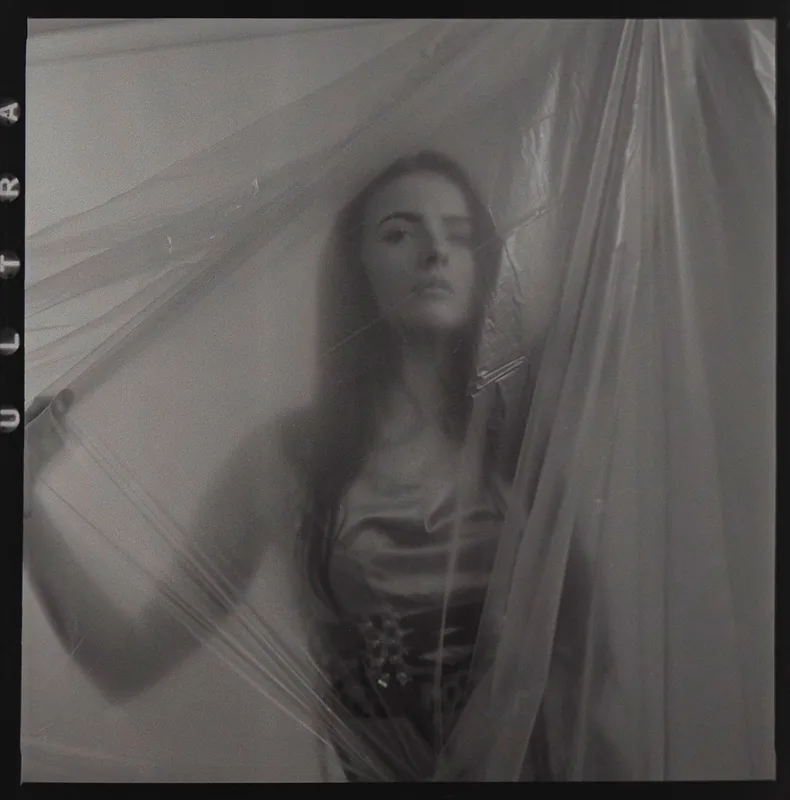 Analoges Schwarz-Weiß-Portrait einer Frau hinter durchscheinendem, fließendem Stoff.