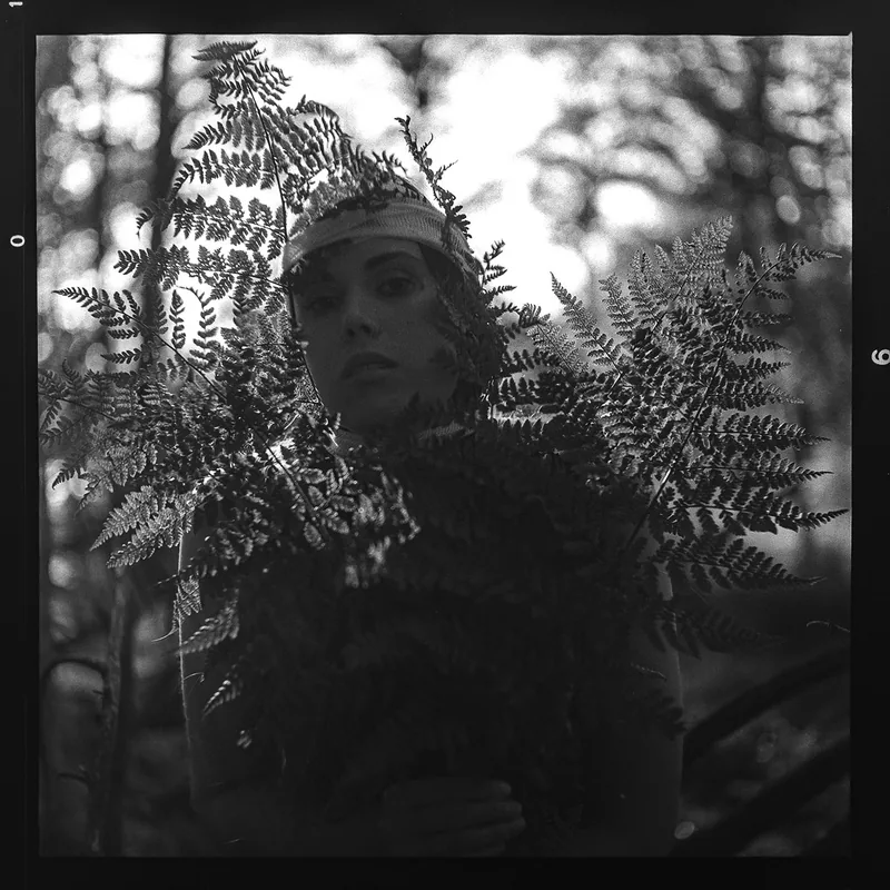 Analoges Schwarz-Weiß-Portrait einer Frau hinter Farnwedeln im Wald