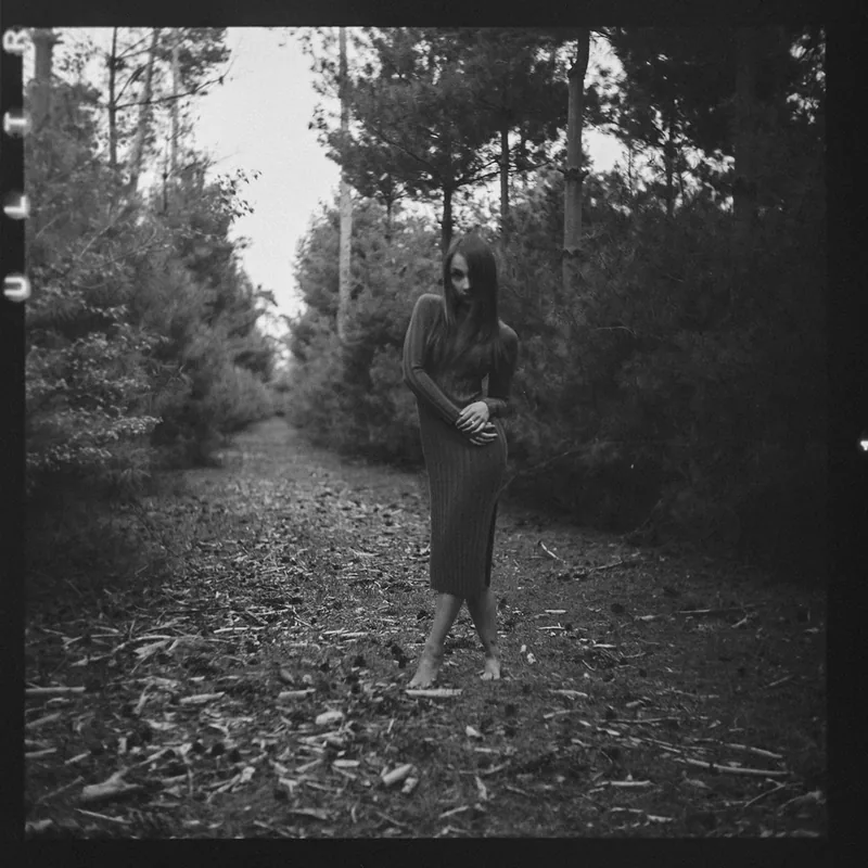 Analoges Schwarz-Weiß-Portrait einer Frau in einem langen Kleid auf einem Waldpfad.