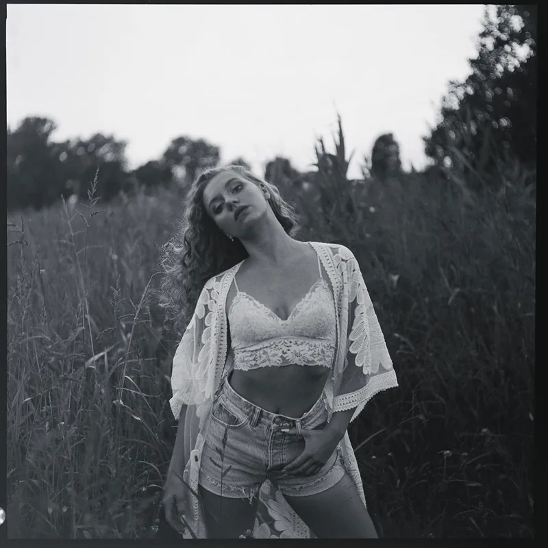 Analoges Schwarz-Weiß-Portrait einer Frau mit lockigem Haar in einem Feld mit hohem Gras.