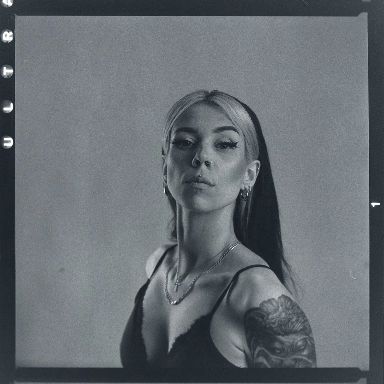 Analoges Schwarz-Weiß-Portrait einer Frau mit Nasenpiercing und Tattoo auf der Schulter.