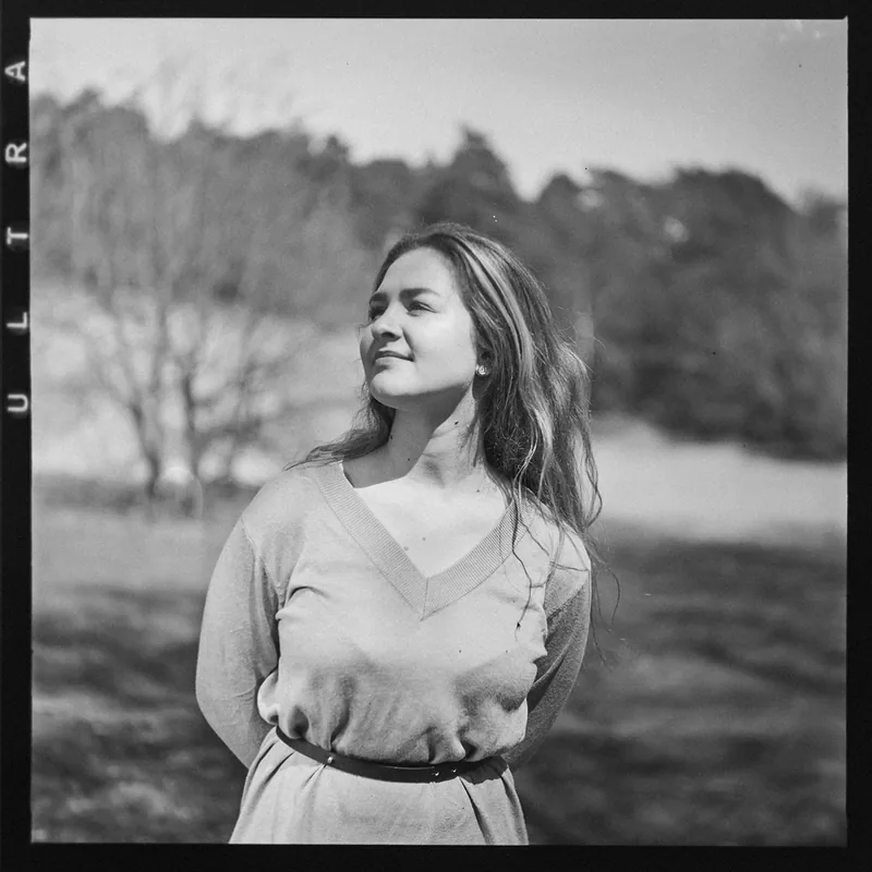 Analoges Schwarz-Weiß-Portrait einer Frau vor einem natürlichen Hintergrund mit Bäumen.