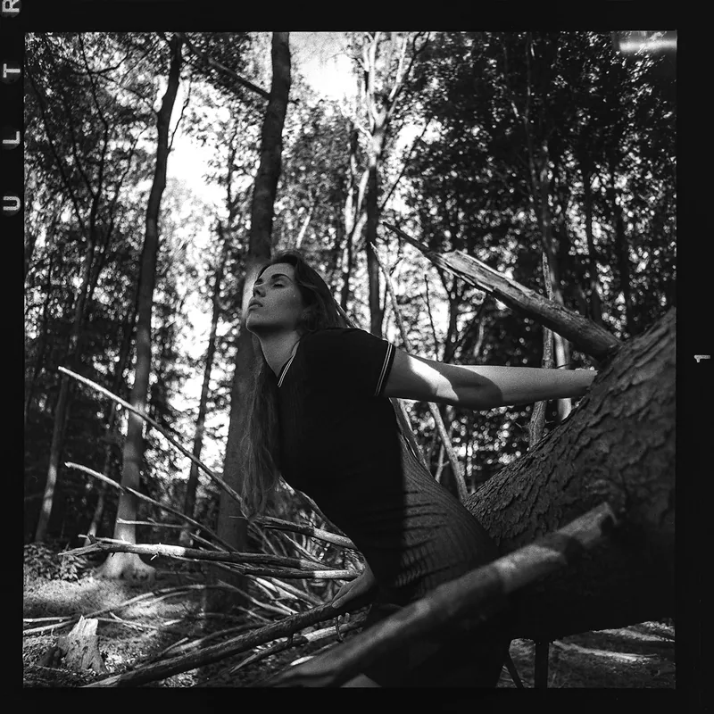 Analoges Schwarz-weiß Portrait einer Frau, die im Wald nach oben blickt.