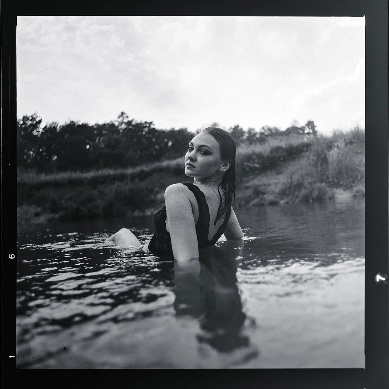 Analoges Schwarz-Weiß-Portrait einer Frau, die im Wasser über die Schulter blickt.