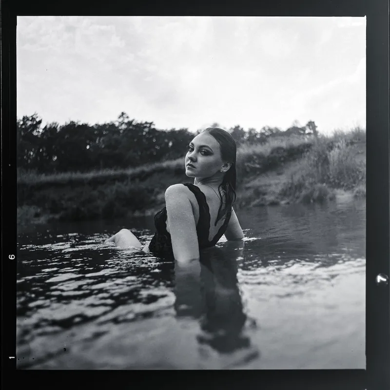 Analoges Schwarz-Weiß-Portrait einer Frau, die im Wasser über die Schulter blickt.