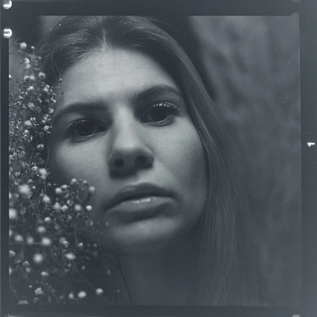 Analoges Schwarz-Weiß-Portrait einer Frau mit zarten Blüten am Bildrand.