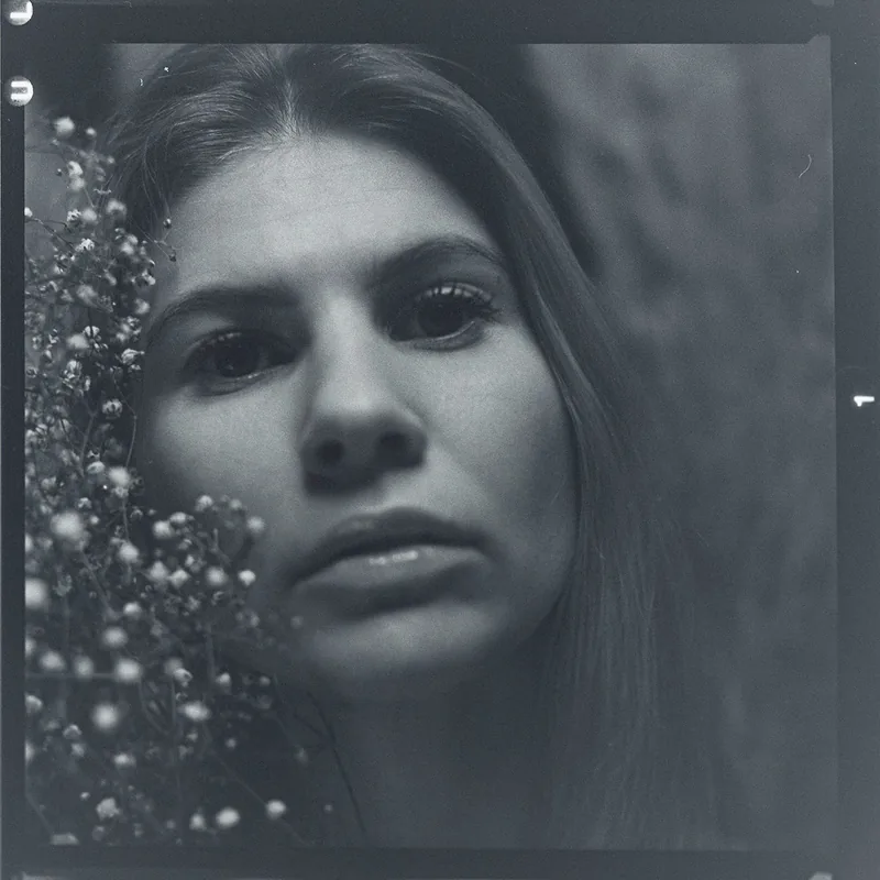 Analoges Schwarz-Weiß-Portrait einer Frau mit zarten Blüten am Bildrand.