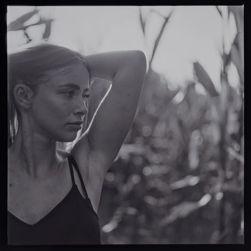 Analoges Schwarz-Weiß-Portrait einer jungen Frau in einem Feld mit hohen Pflanzen.