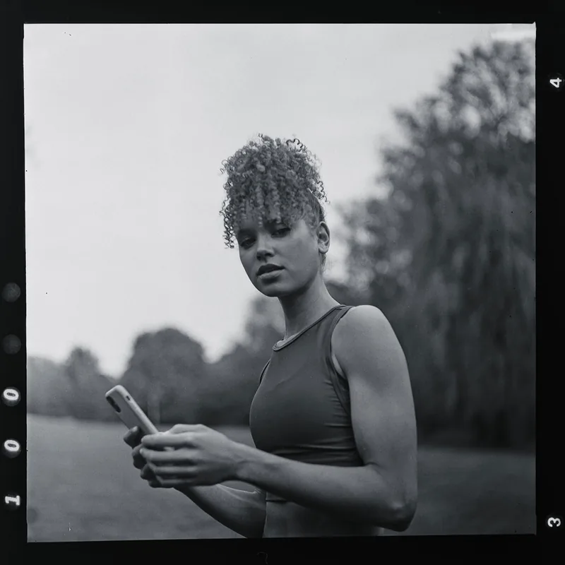 Analoges Schwarz-Weiß-Portrait einer jungen Frau mit lockigem Haar, die ein Smartphone hält.