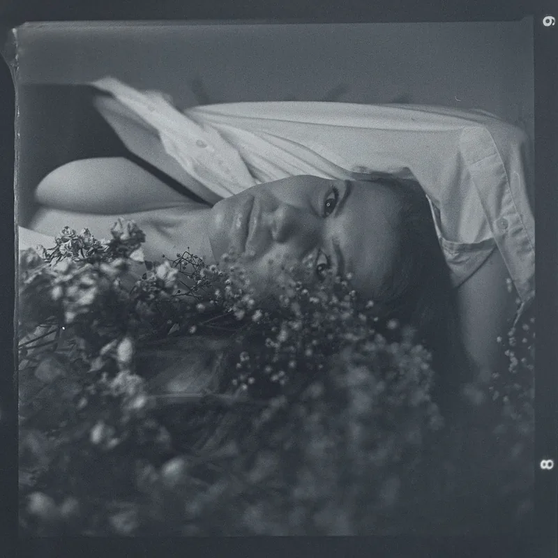 Analoges Schwarz-Weiß-Portrait einer Person hinter zarten weißen Blüten.