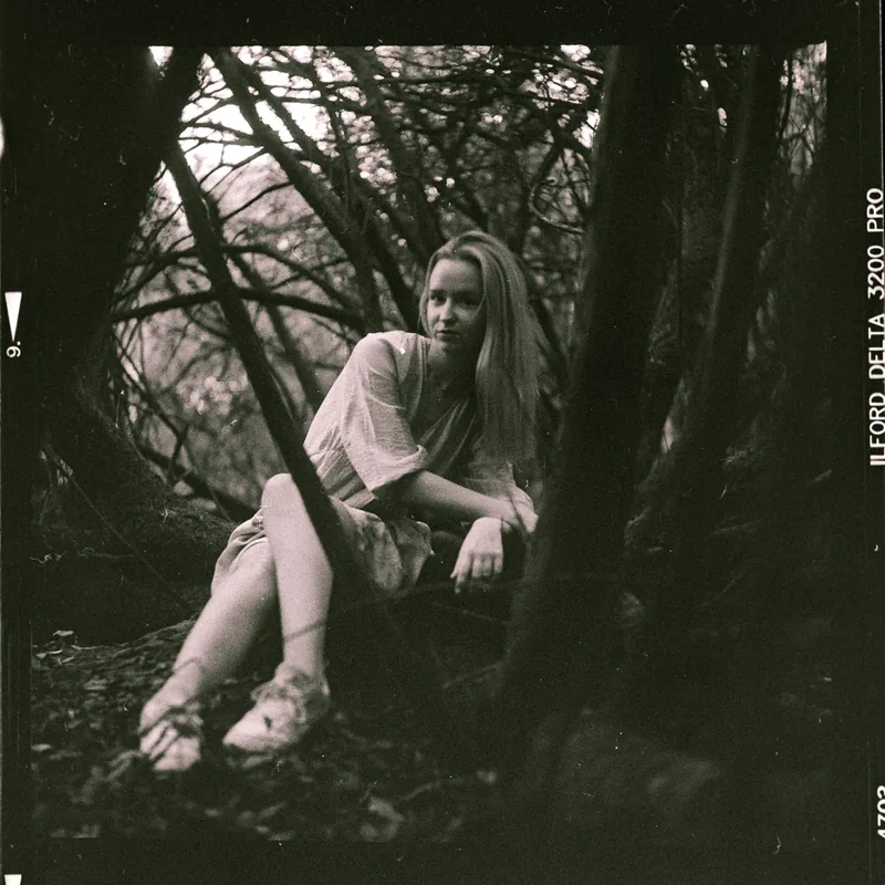 Analoges Schwarz-Weiß-Portrait einer sitzenden Frau inmitten von Bäumen im Wald.